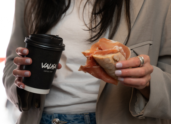 Persona sonriendo con café para llevar en vaso Valka Coffee Stop y bocadillo, pausa de café para llevar.